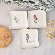 three square dishes with flowers painted on them next to a wooden cutting board and plant