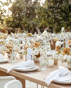 the table is set with white and orange flowers in vases, napkins and plates