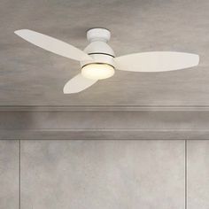 a white ceiling fan mounted on the side of a wall in a room with concrete walls