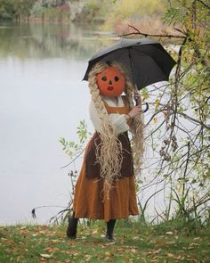 a scarecrow holding an umbrella next to a body of water