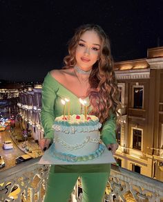 a woman holding a birthday cake with lit candles on it in front of a cityscape