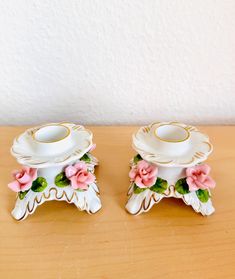 two porcelain dishes with pink flowers on them sitting on a wooden table next to a white wall