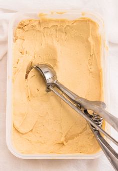 a container filled with yellow cake batter and two silver spoons on top of it