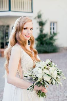 a woman in a wedding dress holding a bouquet of flowers and looking at the camera