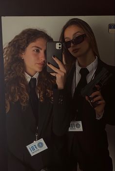 two women in suits are holding up their cell phones to take a selfie with each other