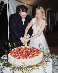 a man and woman cutting into a cake with strawberries on the table next to them