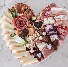 a heart shaped platter filled with different types of cheeses and meats on a marble surface