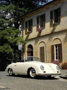 an old white car is parked in front of a building with shutters on the windows