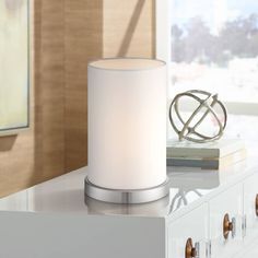 a white candle sitting on top of a table next to a mirror and lamp shade