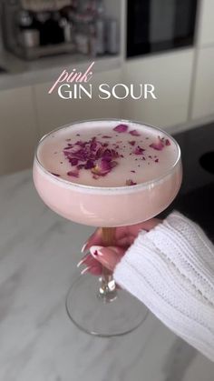 a person holding a drink in a glass with pink flowers on the rim and text gin sour