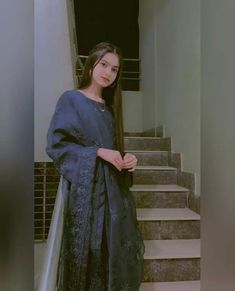 a woman standing in front of some stairs wearing a blue dress and black shawl