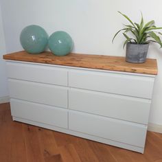 two green balls sit on top of a white dresser next to a potted plant