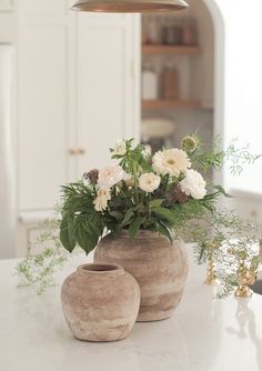 two vases with flowers in them sitting on a kitchen counter next to a lamp