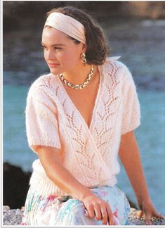 a woman sitting on a rock wearing a white sweater and headband with pearls in her hair