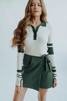 a woman in a green skirt and white sweater posing for the camera with her hands on her hips