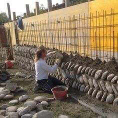 a woman sitting on the ground next to a wall made out of rocks and cement