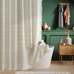 a bath tub sitting next to a green wall with towels hanging on the hooks above it