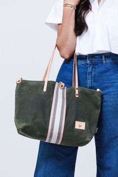 Model displaying brushed leather olive green tote with cream and grey accent stripes down the center and cream colored shoulder straps. Work Bag Essentials, Leather Strap Bag, Wax Canvas, Lynchburg Virginia, Waxed Canvas Bag, Work Tote Bag, Work Tote, Canvas Bags, Webbing Strap