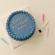 a blue birthday cake with the words happy birthday mark on it next to toothbrushes