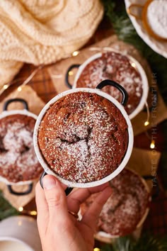 a person holding a cupcake with powdered sugar on top in front of other desserts