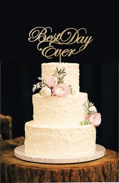 a white wedding cake with pink flowers on top sitting on a wooden table in front of a black backdrop