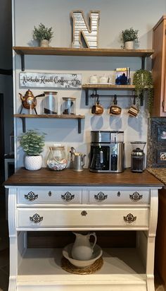 a white kitchen island with coffee maker on top and shelves filled with potted plants