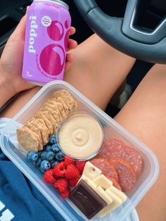 a person is holding a can of soda and some food in their lap while driving