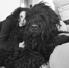 a woman hugging a large black dog on top of a bed