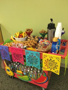 a colorful cart filled with lots of food on top of a carpeted floor next to a green wall