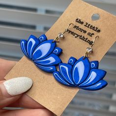 a pair of earrings with blue flowers on them, sitting in front of a card