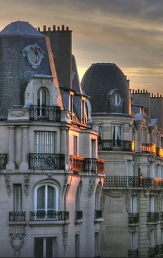 the sun is setting behind some old buildings in paris, with windows and balconies