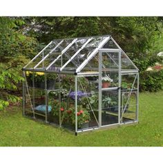 a small greenhouse with plants inside in the grass near some trees and bushes on either side of it