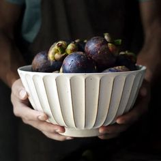 a person holding a white bowl filled with fruit