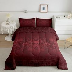 a bed with a red comforter and two pillows on it in a white room