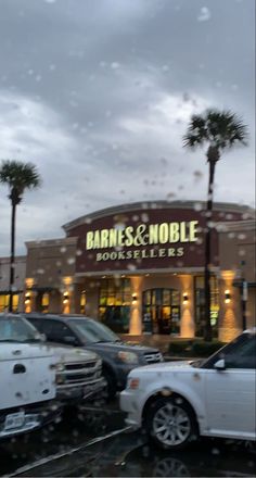 cars are parked in front of a bookmobile with palm trees outside and rain on the windshield