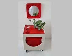 a red and white side table with a plant on it next to a round mirror