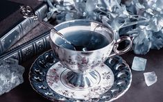 a silver tea cup and saucer on a table with ice cubes next to it