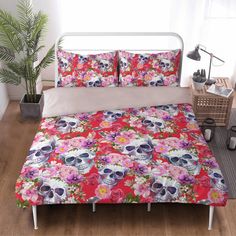 a bed covered in pink and red flowers with skulls on it's head, sitting next to a potted plant