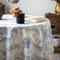 a table topped with a vase filled with flowers next to an open book and candle