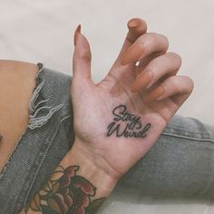 a woman's hand with the word stay weird tattooed on it, and flowers