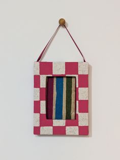 a pink and white frame hanging on a wall with a wooden stick sticking out of it