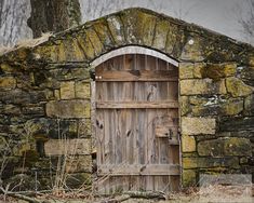 an old stone building with a wooden door in the middle and moss growing on the ground