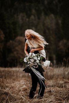 a woman with long blonde hair holding a bouquet of flowers in her hands and walking through tall grass