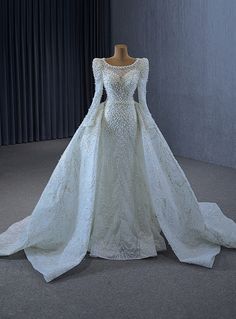 a white wedding dress with long sleeves on display in front of a curtained window