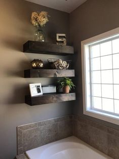 a bath tub sitting under a window next to a shelf filled with flowers and pictures