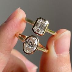 two gold rings with an emerald and diamond set on top, in the palm of someone's hand