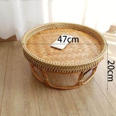 a wicker coffee table with measurements for the top and bottom section, sitting on a wooden floor