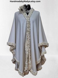 Experience the ultimate luxurious with this handcrafted Embellished Cashmere cape, poncho. Delicately designed with intricate soutache and pearl handwork trim, this shawl is a testament to the skill and craftsmanship of the artisan. The bordered trim adds an original touch, elevating the cape's beauty to a whole new level. This one-of-a-kind piece is perfect for those who appreciate the finer things in life and desire a unique statement accessory. Stay cozy and stylish this winter with this truly exquisite cape. Elegant White Capelet With Cape Sleeves, Elegant Beige Cape Poncho, Elegant Winter Festive Shawl, Elegant Festive Winter Shawl, Elegant Beige Poncho, White Embellished Outerwear For Wedding, Embellished Winter Wedding Outerwear, Elegant White Cape With Cape Sleeves, Winter Wedding Embellished Outerwear