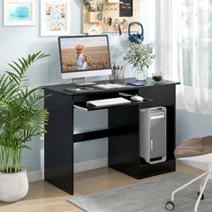 a computer desk with a monitor, keyboard and mouse on it next to a potted plant