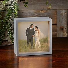 a wedding photo on a wooden table next to a potted plant and vase with greenery